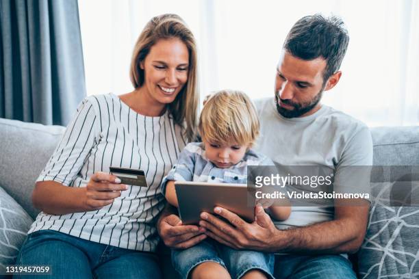 family sitting on the sofa at home and using tablet for online shopping. - booking holiday stock pictures, royalty-free photos & images