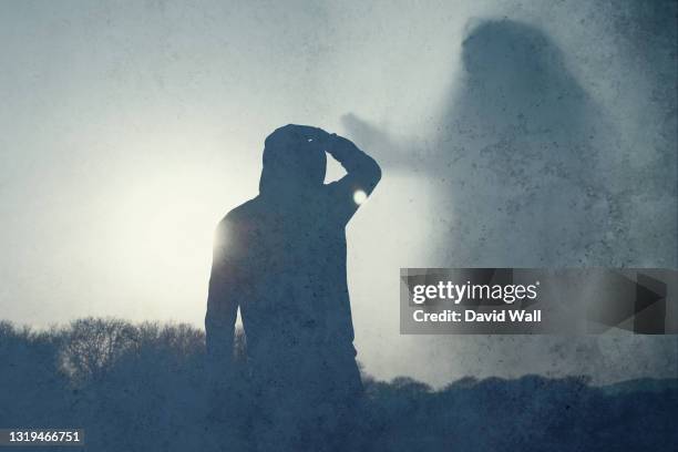 a moody lone hooded figure, back to camera, looking at a giant ghostly figure of a female floating in the sky. with an abstract, grunge, edit. - giant camera stock pictures, royalty-free photos & images