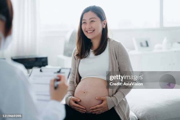 smiling young asian pregnant woman having a consultation with a female doctor during her routine check up at a clinic. check-ups, tests and scans to ensure a healthy pregnancy for both mother and the unborn baby. healthy pregnancy lifestyle - asian pregnancy stock pictures, royalty-free photos & images