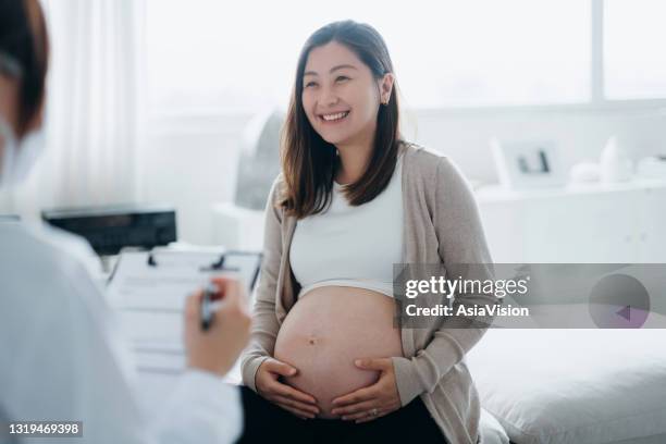 smiling young asian pregnant woman having a consultation with a female doctor during her routine check up at a clinic. check-ups, tests and scans to ensure a healthy pregnancy for both mother and the unborn baby. healthy pregnancy lifestyle - abdomen exam stock pictures, royalty-free photos & images