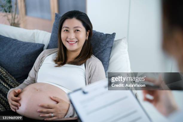 smiling young asian pregnant woman having a consultation with a female doctor during her routine check up at a clinic. check-ups, tests and scans to ensure a healthy pregnancy for both mother and the unborn baby. healthy pregnancy lifestyle - midwife stock pictures, royalty-free photos & images
