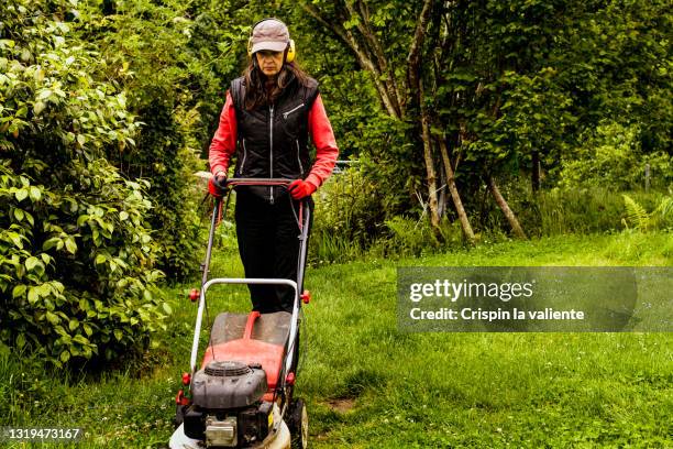 the woman with protective headphones pushing lawn mower in her garden - cutting grass stock pictures, royalty-free photos & images