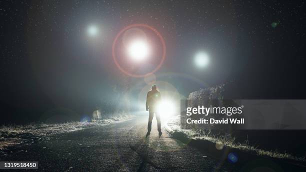 ufo concept. glowing orbs, floating above a misty road at night. with a silhouetted figure looking at the lights. - flying saucer stock pictures, royalty-free photos & images