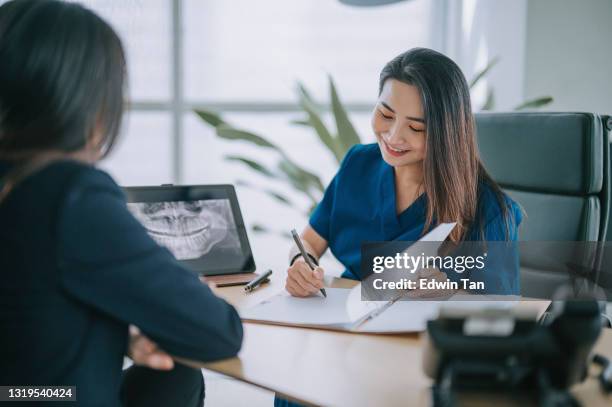 dentista chinesa asiática explicando imagem de raio-x médico para uma paciente do sexo feminino em seu consultório - implante dentário - fotografias e filmes do acervo