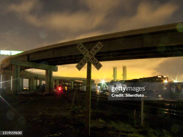 freight train passes underneath elevated freeway - train yard at night stock pictures, royalty-free photos & images