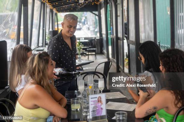 Waiter without a mask pours champagne for customers during the "Eggs and Leggs Drag Brunch" at Da Capo on the Upper West Side on May 22, 2021 in New...