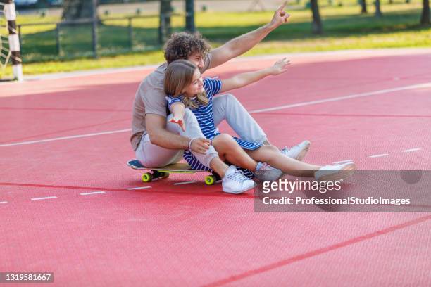 young father is having fun with his daughter while they riding a skateboard together. - father longboard stock pictures, royalty-free photos & images