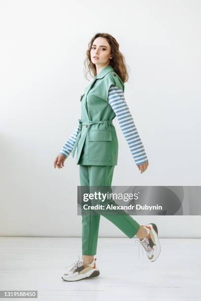 woman model in green stylish suit posing making a step and looking at the camera - tree on white stockfoto's en -beelden