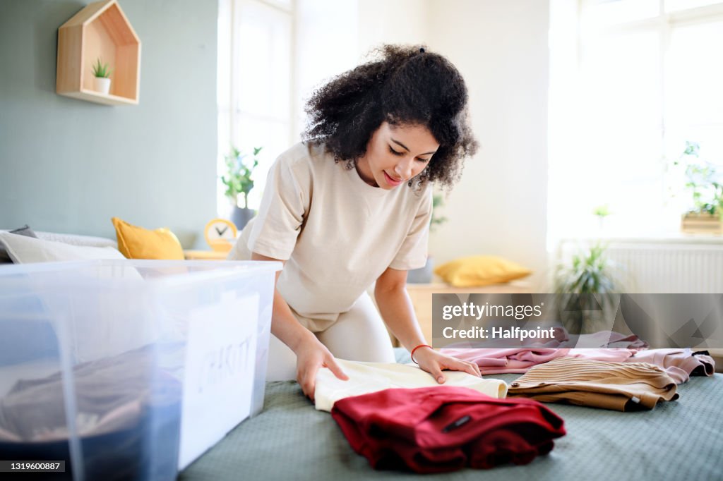 Young woman sorting wardrobe indoors at home, charity donation concept.