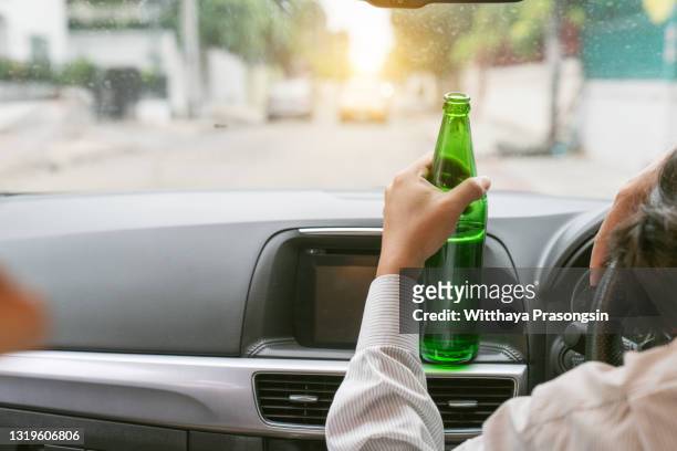 drunk asian young man drives a car with a bottle of beer with sunset background - drunk driving accident stock pictures, royalty-free photos & images