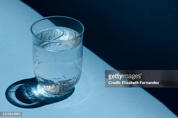close-up of a glass of water shining in the sunlight on a bright blue background - vaso de agua fotografías e imágenes de stock