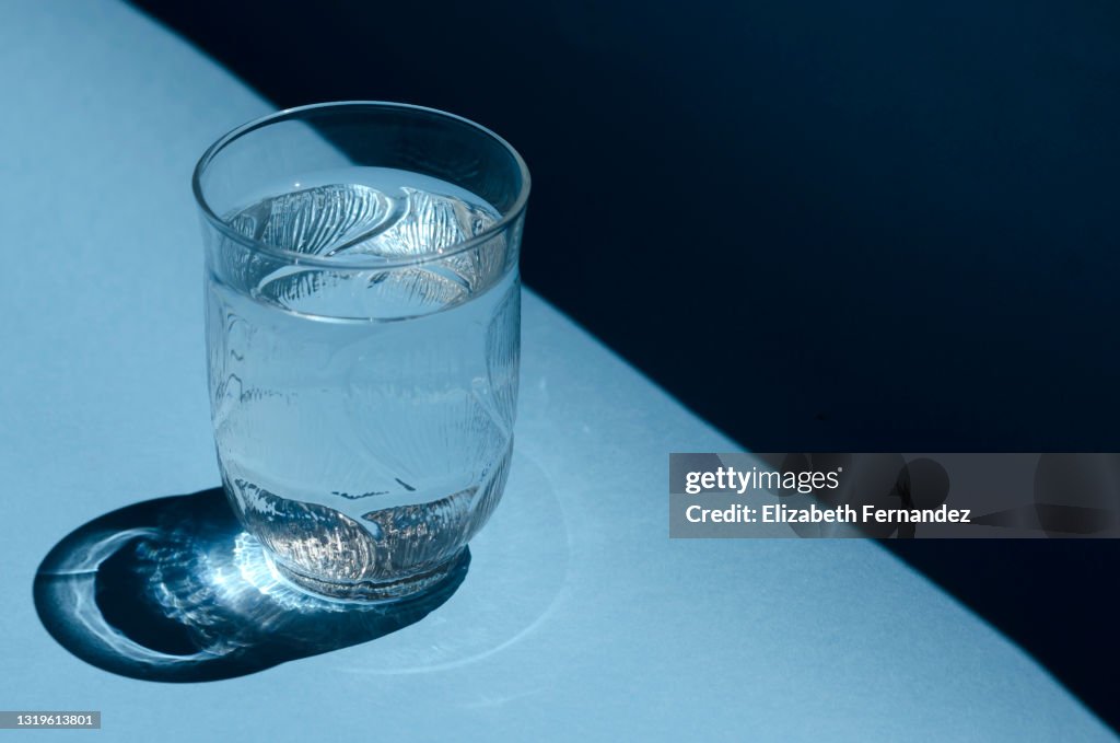 Close-up of a glass of water shining in the sunlight on a bright blue background