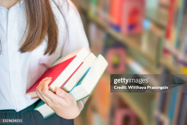 hand in a white shirt student holding a book in the library to study her classmate's research - an educational concept. - textbook stock pictures, royalty-free photos & images