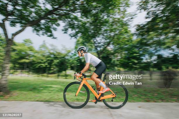 side view asian chinese female professional cyclist athlete sportsman sprinting cycling in public park - adult riding bike through park stock pictures, royalty-free photos & images