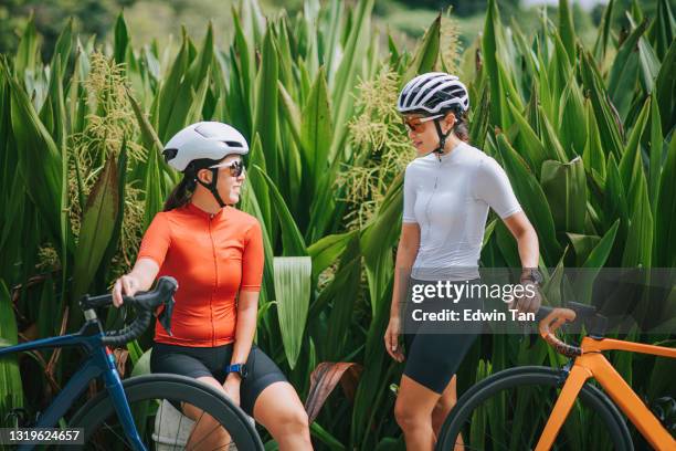 2 asian chinese woman road bike cyclist side by side at public park in the morning resting talking - camisola de ciclismo imagens e fotografias de stock