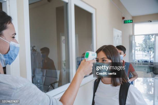 teacher checking temperature of students with face mask for pandemic while children go back to school - teacher taking attendance stock pictures, royalty-free photos & images