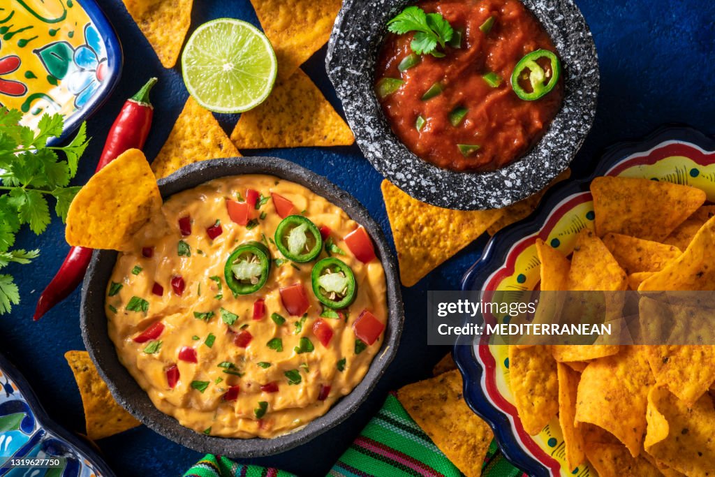 Cheedar cheese dip and Mexican tomato salsa dip with nacho chips on dark blue