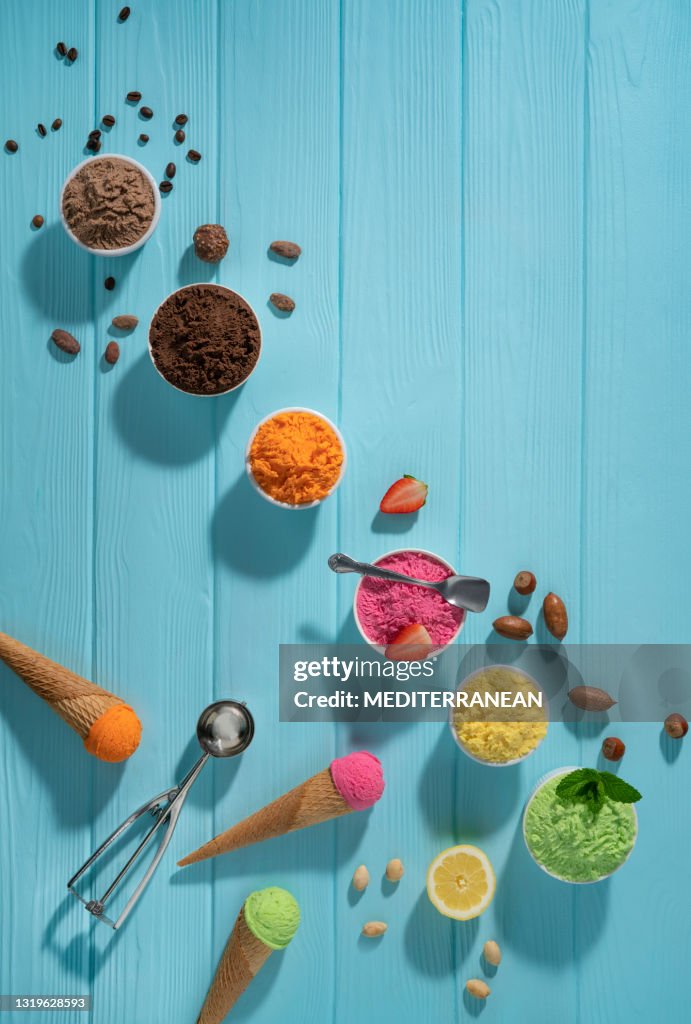 Assorted ice cream cups in a row and waffle cones colorful on blue wood background