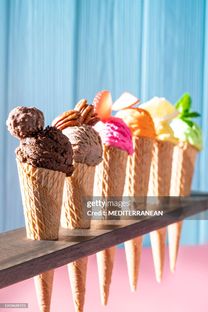 Assorted ice cream waffle cones in a row colorful different flavor on pink and blue wood