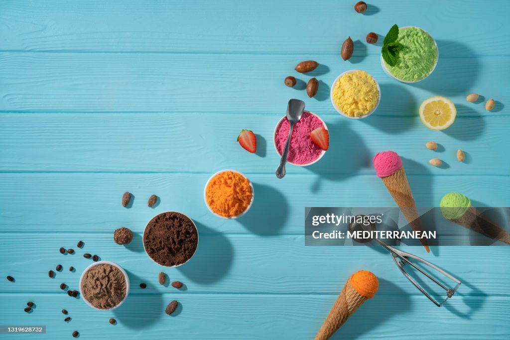 Assorted ice cream cups in a row and waffle cones colorful on blue wood background