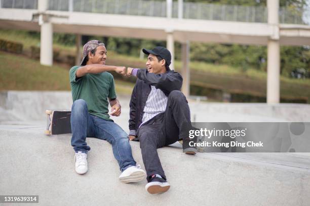 patinadores asiáticos sentados tomando un descanso y hablando en el parque de skate - fist bump fotografías e imágenes de stock
