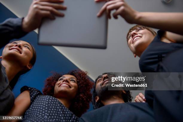 smiling international male and female professionals looking away while holding digital tablet in office - group of businesspeople standing low angle view stock pictures, royalty-free photos & images