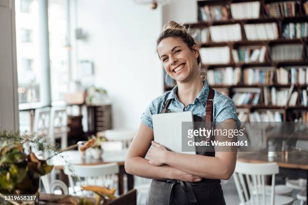 cheerful mid adult waitress holding digital tablet at cafe - kellner stock-fotos und bilder