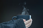 Hands of young girl with a hot Cup of tea on a dark background. Steam rises from the hot drink.