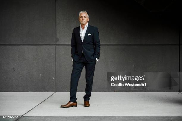 businessman in front of gray wall - ganzkörperansicht stock-fotos und bilder
