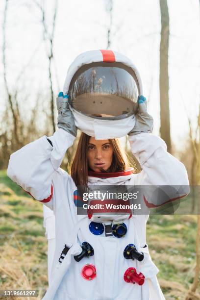 female astronaut removing space helmet in forest - space helmet stock-fotos und bilder