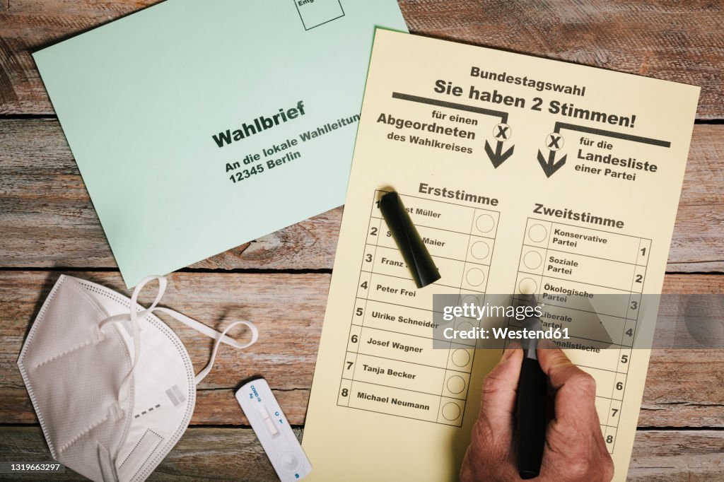 Hand checking ballot for federal elections by mail on table with protective mask and corona rapid test