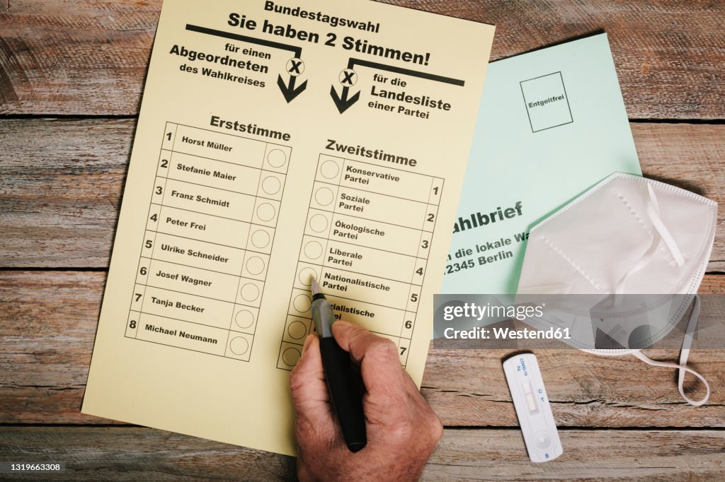 Hand checking ballot for federal elections by mail on table with protective mask and corona rapid test