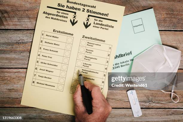 hand checking ballot for federal elections by mail on table with protective mask and corona rapid test - stembiljet stockfoto's en -beelden