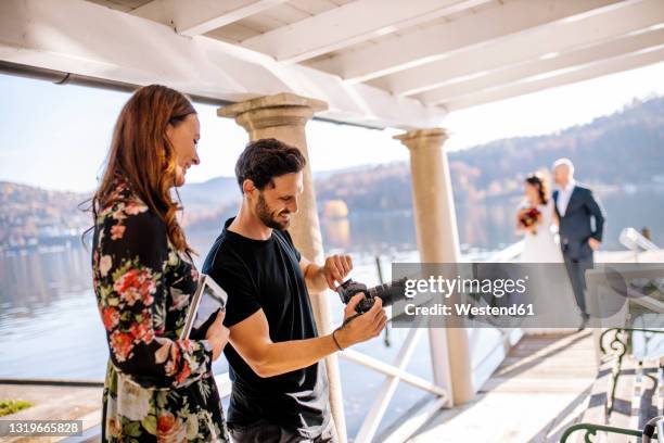 photographer and wedding couple on jetty over lake - wedding photographer stock pictures, royalty-free photos & images