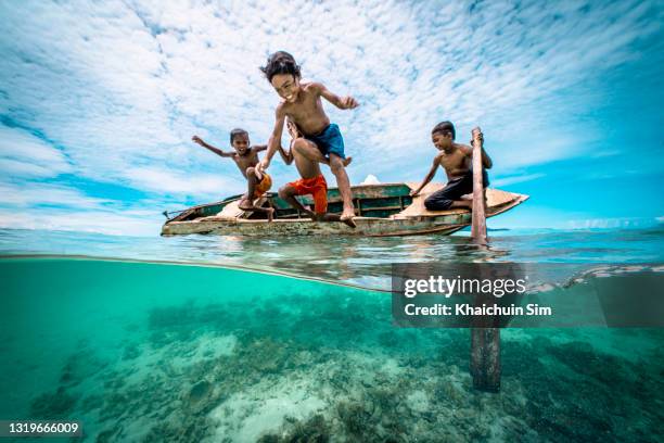 bajau children jumping off a wooden canoe in the sea of tropical island beach - kids fun indonesia stock pictures, royalty-free photos & images