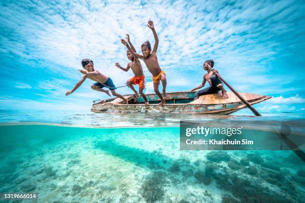 bajau children jumping off a wooden canoe in the sea of tropical island beach - irian jaya photos et images de collection