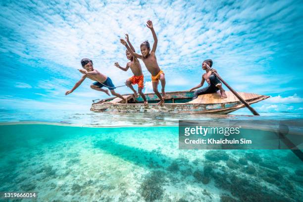 bajau children jumping off a wooden canoe in the sea of tropical island beach - papuma beach stock pictures, royalty-free photos & images