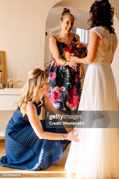 smiling woman giving bouquet to bride in domestic room - bruidsmeisje stockfoto's en -beelden