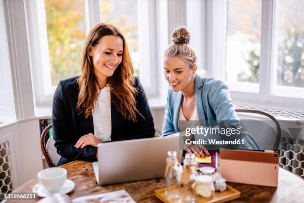 businesswomen discussing over laptop at office - organizador de eventos fotografías e imágenes de stock