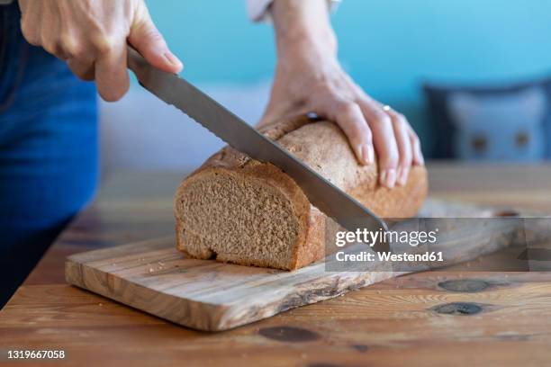 woman cutting loaf of bread on cutting board at home - bread knife stock-fotos und bilder