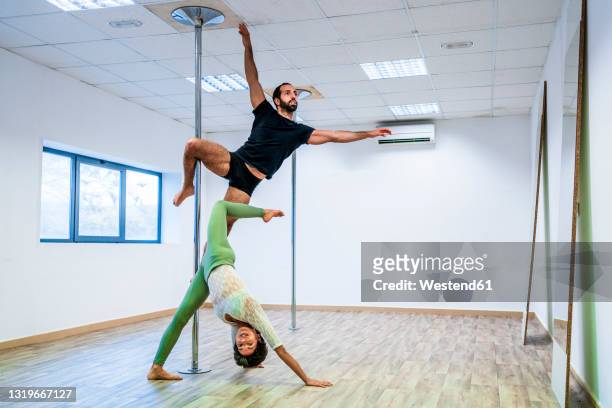 male and female dancers stretching while practicing on rod in dance studio - pole dance stock pictures, royalty-free photos & images