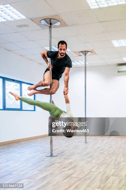male acrobat supporting woman while holding hands during rehearsal on rod in dance studio - stangentänzerin stock-fotos und bilder