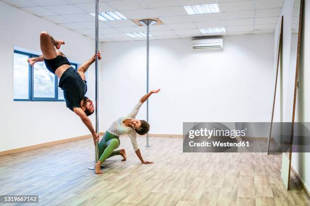 mid adult male acrobat balancing on rod by woman in dance studio - pole dance fotografías e imágenes de stock