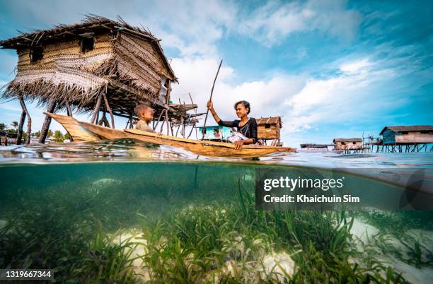 bajau woman rowing wooden canoe in floating village carrying her child - itinerant stock-fotos und bilder