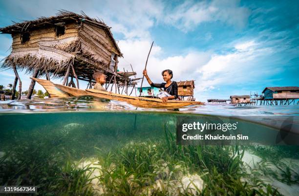 bajau woman rowing wooden canoe in floating village carrying her child - zeegras stockfoto's en -beelden