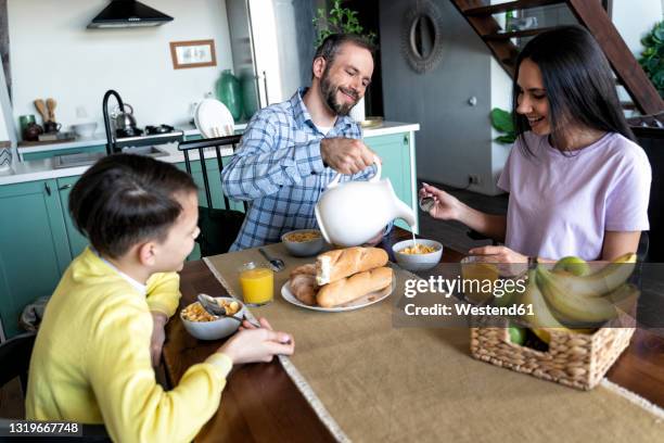 father pouring milk while having breakfast with family at home - mother son milk imagens e fotografias de stock