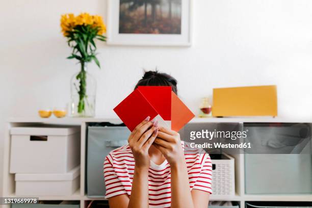 young woman holding red color swatch in front of face at home - color chart stock-fotos und bilder