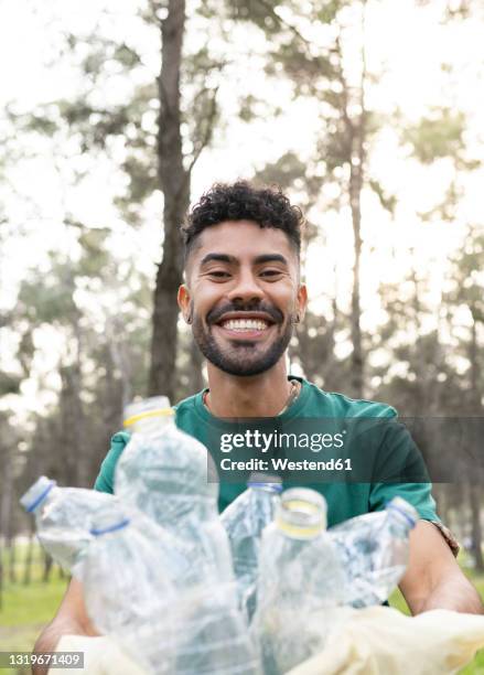 smiling young male volunteer collecting plastic bottles in forest - environmental cleanup stock pictures, royalty-free photos & images