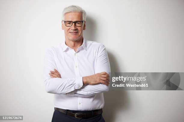 mature businessman standing with arms crossed in front of white wall - chemise blanche photos et images de collection