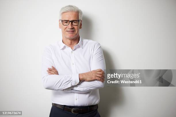 mature businessman standing with arms crossed in front of white wall - person standing infront of wall stockfoto's en -beelden